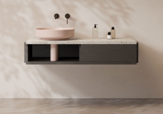La collezione di arredi e specchi LARI di Alice, con design Studio àr-o propone modelli con vani a vista. Il mobile lavabo in foto nella finitura Ebano Antracite ha top in Marmoresina Fior di Pesco Grey. È abbinato al lavabo tondo da appoggio FORM Ø45 in finitura Rosa matt con coprisifone in tinta ed è dotato di cassetto push-pull laterale a destra. Misura L 120 x H 25 cm. www.aliceceramica.com – Salone del Mobile 2026, padiglione Pad. 6, Stand C42.