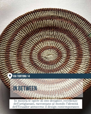 Mostra “In Between” in via Tortona 14 per il Fuorisalone 2026. In primo piano un oggetto artigianale circolare intrecciato a mano, con motivo concentrico nei toni del beige e del marrone. La slide presenta opere di otto designer che raccontano l’identità dell’Ecuador attraverso il design contemporaneo e l’artigianato d’eccellenza.