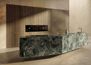 La cucina 36e8 Formae di Lago si sviluppa intorno all'isola monolitica, dalla presenza scultorea e scenografica, in Xglass verde alpi lucido con  le venature che scorrono senza interruzioni tra frontali e piano. I sottioli piedini sollevano e alleggeriscono la composizione. Il sistema si arricchisce di nuovi materiali ad alte prestazioni, pensati per un utilizzo quotidiano, come le superfici strutturate per i frontali di basi e colonne realizzate in laminati nelle finiture cemento o legno cannettatto.  https://www.lago.it - EuroCucina 2026, padiglione 24, Stand D06,D08.