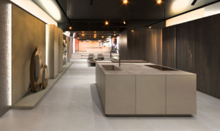 La cucina Ak_Project con sistema Lift e nuovi sistemi Feeling Home di Arrital rafforza il dialogo tra i sistemi cucina e la zona living sottolineando la continuità tra funzione e comfort. La finitura laccato Iron costruisce un piano materico compatto e sofisticato, capace di assorbire la luce e restituirla con misura. Attraverso la boiserie Planar in Noce Carbo la parete si trasforma non solo in un'architettura, ma in un elemento attivo che connette le funzioni fino a integrarsi nel Pass System, una soluzione che separa senza interrompere, definendo un passaggio fluido e continuo tra la cucina e il living. https://www.arrital.it - Fuorisalone, Showcase Arrital – Corso Europa 22, Milano.