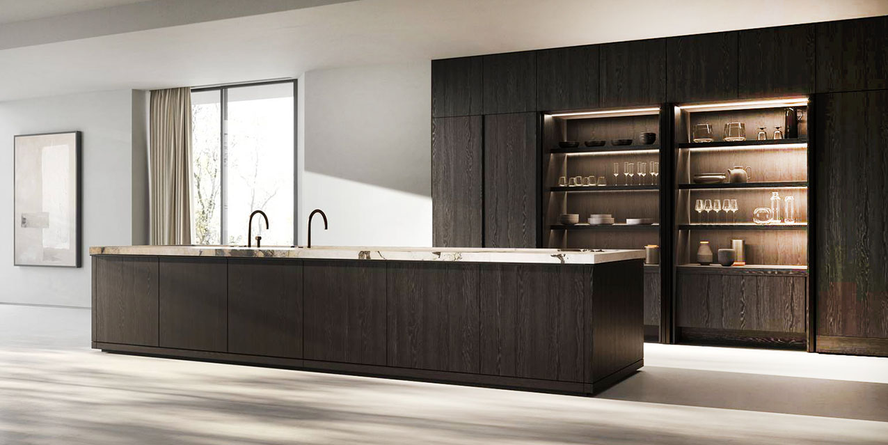 L'isola con una grande presenza scenica domina la composizione Methis di Key Cucine: è realizzata in rovere fossile coffee, con un piano in marmo calacatta iron attraversato da venature profonde che richiamano il legno. Il piano di lavoro introduce una nuova ergonomia, con un ribassamento dedicato alla preparazione e un sistema di scanalature che permette agli accessori di scorrere e sovrapporsi. Alle spalle, trova posto la boiserie in grigio cemento. https://www.keysbabo.com - Fuorisalone, Showroom Agape Milano – Via Statuto 12, Milano.