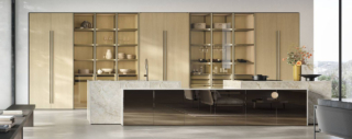 La composizione nata dall'incontro tra Natural e Aliant di Stosa si sviluppa in nuove verticalità grazie all'introduzione di colonne, nella nuova finitura Rovere Sabbia, che celano interni accessoriati dietro alle ante intere retrattili. L'isola operativa ha un volume scultoreo, alleggerito dalle basi con piedini ridotti, ed è rivestita in Neolith Taj Mahal e specchio Bronzo. La nuova boiserie Symetra, con luce perimetrale integrata che esalta la matericità delle superfici, e le uove armadiature living con anta intera completano la zona operativa. https://www.stosacucine.com - EuroCucina 2026, padiglione 04, Stand C02,D02,D01.