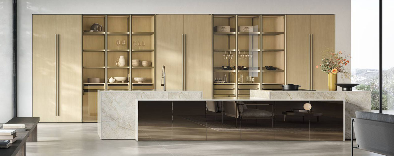 La composizione nata dall'incontro tra Natural e Aliant di Stosa si sviluppa in nuove verticalità grazie all'introduzione di colonne, nella nuova finitura Rovere Sabbia, che celano interni accessoriati dietro alle ante intere retrattili. L'isola operativa ha un volume scultoreo, alleggerito dalle basi con piedini ridotti, ed è rivestita in Neolith Taj Mahal e specchio Bronzo. La nuova boiserie Symetra, con luce perimetrale integrata che esalta la matericità delle superfici, e le uove armadiature living con anta intera completano la zona operativa. https://www.stosacucine.com - EuroCucina 2026, padiglione 04, Stand C02,D02,D01.