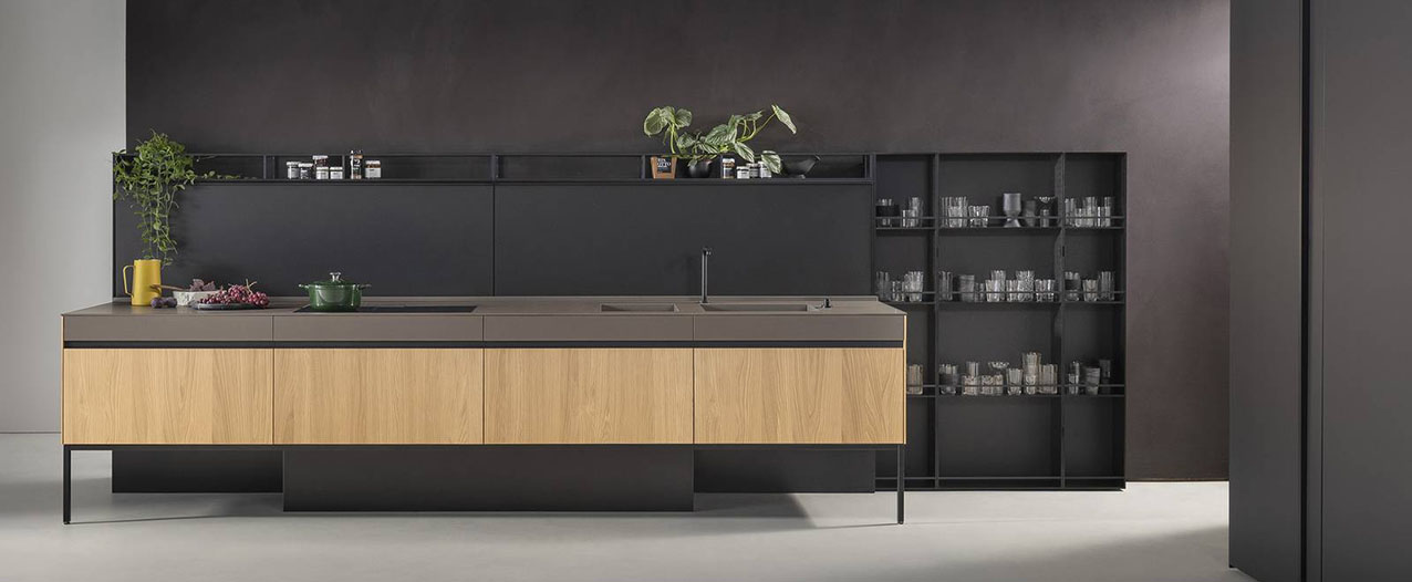 Leggera ed elegante l'isola della cucina Sei di Euromobil che è attrezzata con il piano cottura e la zona lavaggio; le basi sollevate da terra hanno le ante impiallacciate castagno sabbiato light e il piano in Fenix Bronzo Doha. Al posto dei pensili trova posto lo schienale in Fenix Nero Ingo con mensole coordinate e integrate. Un modulo base da 60 cm, prezzo a partire da 590 euro + Iva. https://www.euromobil.com