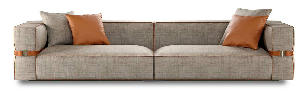 Il divano B.E.L.T. di Turri è caratterizzato dalla presenza di una cintura in pelle intrecciata, con una fibbia personalizzata con il monogramma “T” dell'azienda, che avvolge i braccioli e da una forma compatta e squadrata; è rivestito in tessuto con profili sartoriali e piping in pelle. https://turri.it - Salone del mobile 2026, padiglione 09, Stand H11, L10.