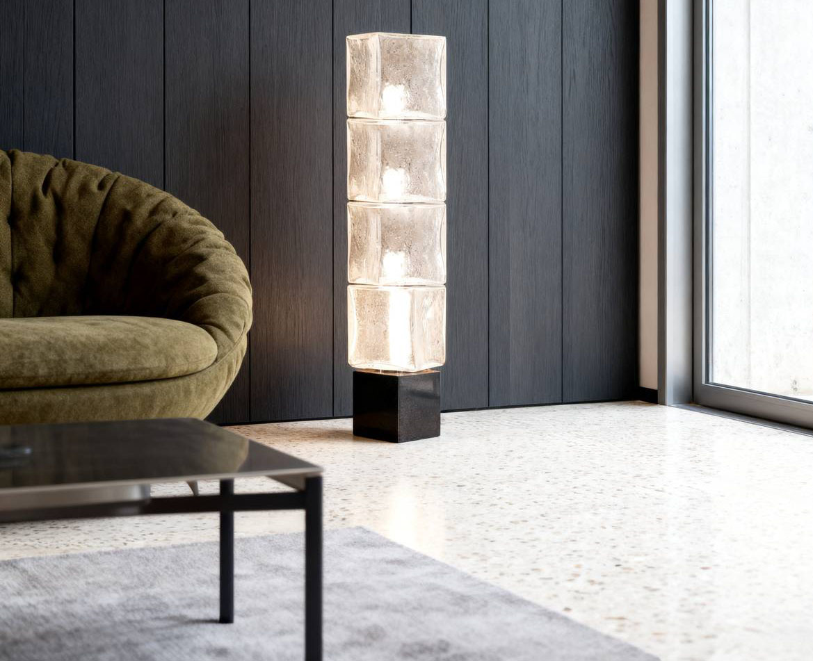 La lampada da terra On the Rocks di Venini ha una base monolitica in marmo nero Zimbabwe su cui poggiano una serie di cubi in vetro di Murano soffiato a mano. I moduli in vetro sono prodotti con la tecnica del pulegoso che prevede l’inclusione di minute bolle d’aria all’interno della massa vitrea; questo processo, custodito dai maestri vetrai,  dona alla superficie un carattere poroso, quasi geologico, e permette alla luce di filtrare con una luminosità sottile e organica. ttps://www.venini.com - Salone del mobile 2026, padiglione 09, Stand C05.