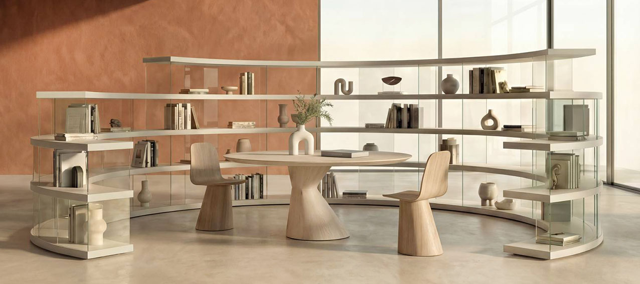 La libreria Air Roundy di Lago ha un'insolita forma curva ed è composta da una serie di mensole, nelle finiture laccato Havana e Tortora, sostenute dal vetro che sembrano fluttuare nello spazio. Le curvature con raggi differenti permettono di dare vita a soluzioni di dimensioni diverse.   https://www.lago.it - Salone del mobile 2026, padiglione 24, Stand D06, D08.