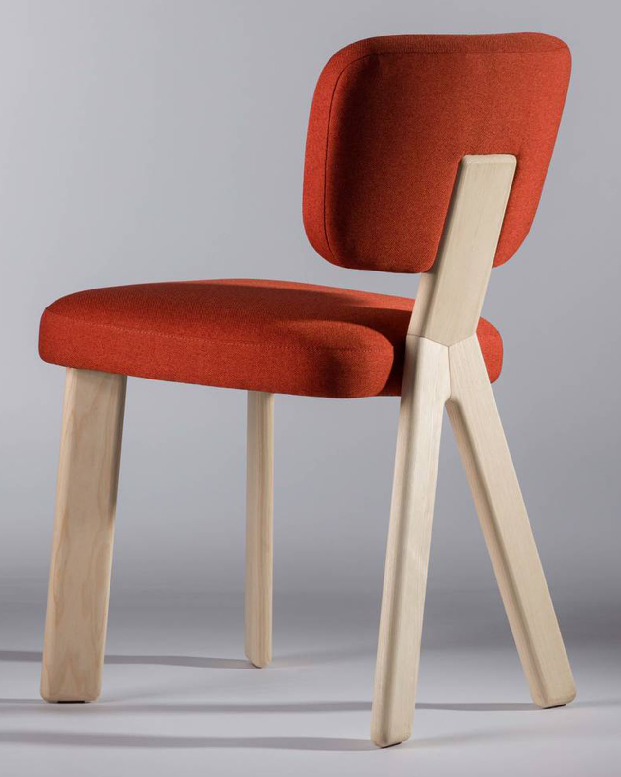 La sedia Nuy di Et al. ha la struttura in legno di frassino ed è imbottita e rivestita in tessuto rosso; le gambe posteriori, a forma di Y rovesciata, la rendono riconoscibile e stabile. https://www.et-al.it/it - Salone del mobile 2026, padiglione 18, Stand D27.