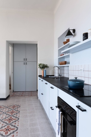 Cucina con pavimento e rivestimento in gres effetto graniglia, dove i tappeti decorativi in piastrelle e le campiture in tinta unita aiutano a mimetizzare fuori squadra e pareti inclinate, presenti nel progetto, trasformando i vincoli architettonici in un elemento progettuale. Progetto architetto Clara Bona.