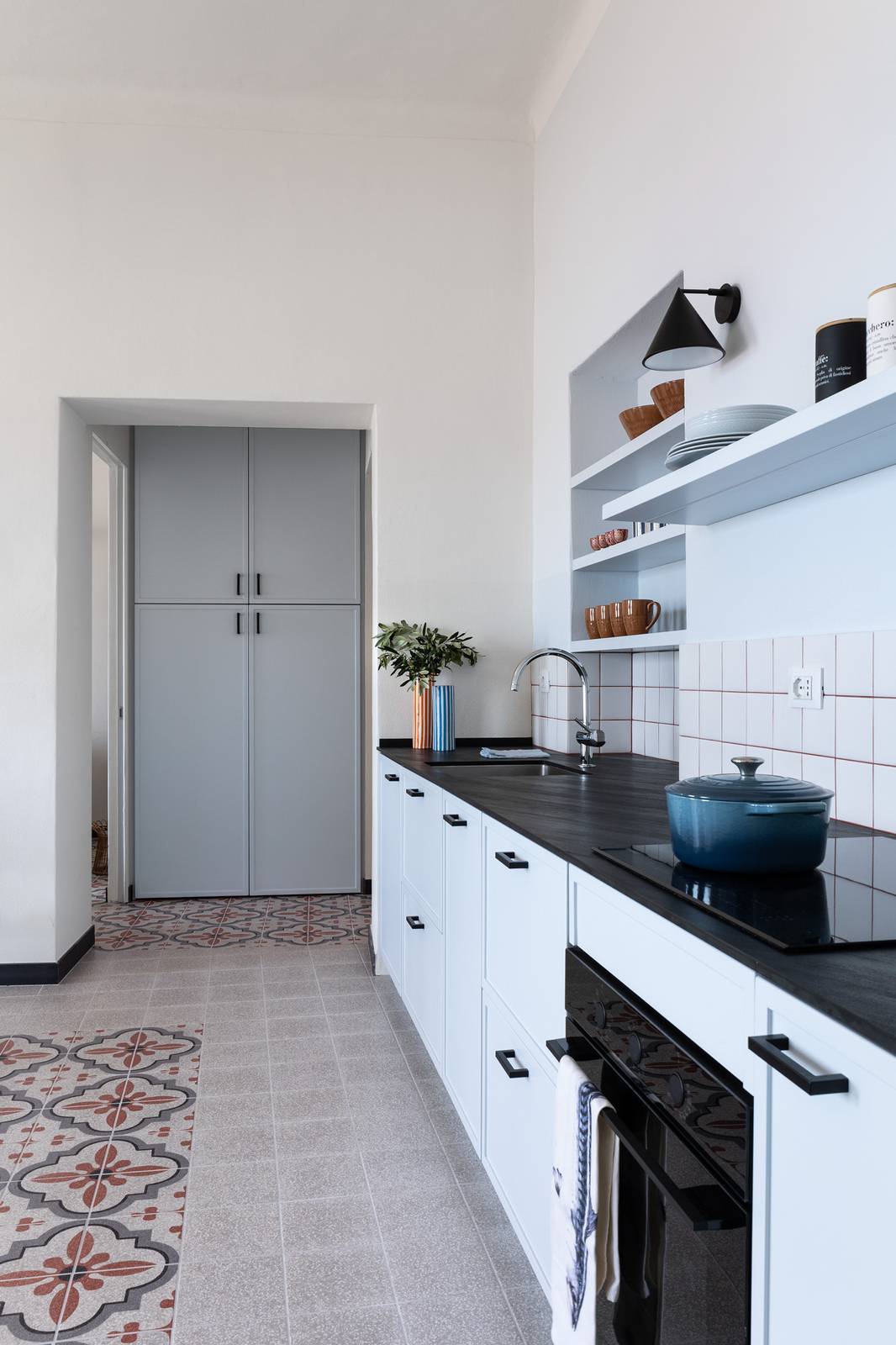Cucina con pavimento e rivestimento in gres effetto graniglia, dove i tappeti decorativi in piastrelle e le campiture in tinta unita aiutano a mimetizzare fuori squadra e pareti inclinate, presenti nel progetto, trasformando i vincoli architettonici in un elemento progettuale. Progetto architetto Clara Bona.