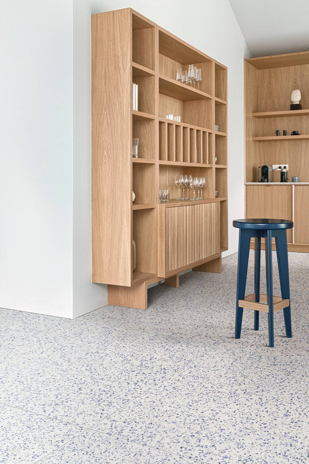 Ambiente giorno con mobile in legno e sgabello blu, pavimento in gres Marazzi Frammento effetto graniglia grigio blu