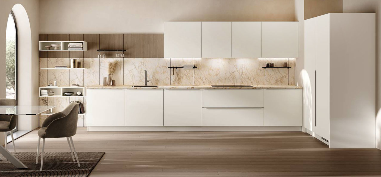 Un ambiente luminoso e fresco con la cucina ad angolo Moda di Scavolini che ha le ante lisce realizzate in PET Bianco Talco abbinate al piano e agli schienali in gres porcellanato Cristallo Macchiavecchia. La boiserie Vertical System in impiallacciato Rovere Dune può essere attrezzata con elementi diversi. Prezzo su richiesta. https://www.scavolini.com