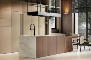 Legno scuro e marmo venato per la scultorea isola della composizione Daytona di Arrex Le Cucine che integra lateralmente un tavolo snack con il piano in impiallacciato Rovere Rhum. Il piano di lavoro e il supporto del piano snack sono realizzati in pregiato Marmo Taj Mahal; le ante delle basi sono in legno nella lavorazione rigata. Le colonne dell'armadiatura sono in PET Gold. Un modulo base da 60 cm, prezzo 618 euro + IVA. https://www.arrex.it Legno scuro e marmo venato per la scultorea isola della composizione Daytona di Arrex Le Cucine che integra lateralmente un tavolo snack con il piano in impiallacciato Rovere Rhum. Il piano di lavoro e il supporto del piano snack sono realizzati in pregiato Marmo Taj Mahal; le ante delle basi sono in legno nella lavorazione rigata. Le colonne dell'armadiatura sono in PET Gold. Un modulo base da 60 cm, prezzo 618 euro + IVA. https://www.arrex.it