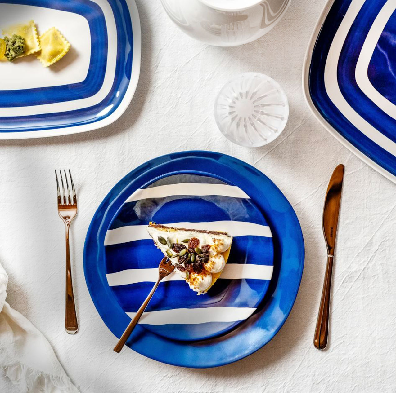 Fanno parte della collezione Riviera di Fratelli Guzzini i piatti in melamina nelle varianti blu intenso o con uno scenografico decoro a righe bianche e blu. Sono leggeri, facili da usare e lavabili in lavastoviglie. Sono posizionati su una tovaglia candida che sottolinea lo stile marinaro della tavola. Il piatto dessert a righe misura Ø 21,5 cm, prezzo 6,90 euro. Il piatto piano blu misura Ø 27,5 cm, prezzo 8,90 euro. https://guzzini.com