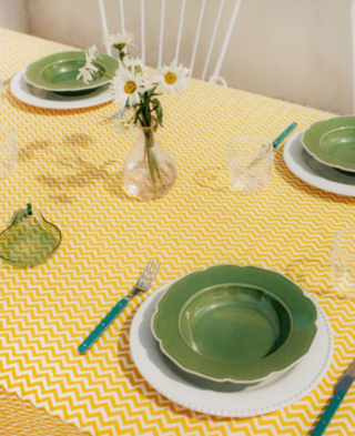 Una tavola allegra e informale con i piatti onde verde di Mango Home abbinati a  un piatto piano bianco e posizionati su una tovaglia con un motivo a zig zag giallo. Sono realizzati in 100% gres porcellanato disponibili in tre varianti di colore. Misurano Ø 22,5 cm. Prezzo 12,99 euro cad. https://shop.mango.com