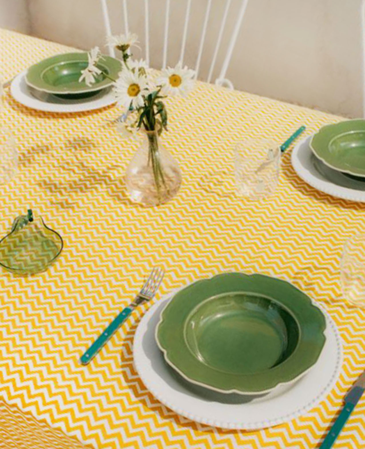 Una tavola allegra e informale con i piatti onde verde di Mango Home abbinati a  un piatto piano bianco e posizionati su una tovaglia con un motivo a zig zag giallo. Sono realizzati in 100% gres porcellanato disponibili in tre varianti di colore. Misurano Ø 22,5 cm. Prezzo 12,99 euro cad. https://shop.mango.com
