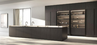 Rovere Fossile Coffee per le ante dell'isola e delle colonne nella composizione Methis di Key Cucine. Le colonne a parete accolgono due nicchie con una boiserie attrezzata con lo schienale nella finitura grigio cemento; il piano è realizzato in pregiato marmo calacatta iron e ospita il lavabo doppio. Prezzo su richiesta. https://www.keysbabo.com