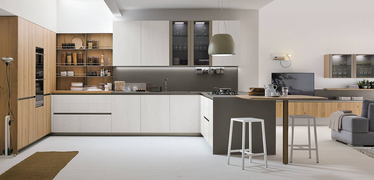 Stile scandinavo per la cucina angolare, che si apre completamente sulla zona giorno, Natural di Stosa che accosta le ante delle basi e dei pensili in Rovere Bianco a quelle delle colonne in Rovere Miele. La penisola dalle dimensioni contenute è dotata di un piano snack in appoggio sul top in pietra Neolith®. I pensili sono dotati di ante in vetro con il telaio nella finitura Titanio. Prezzo su richiesta. https://www.stosacucine.com