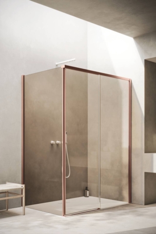 Box doccia VENTO della linea Ibra Showers con configurazione ad angolo con porta scorrevole, vetro fisso in linea e vetro laterale. Profili e dettagli in finitura Rame Spazzolato, vetro trasparente da 8 mm. In abbinamento, piatto doccia Synthesis in Tekorstone Bianco L 160 x P 80 cm.
