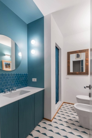 In questo bagno da un lato è stato scelto un colore intenso, l’ottanio, con cui è stata dipinta la nicchia del lavabo, che è stato ripreso anche per il mobile in legno cannettato e per la tenda della doccia. Dall’altra parte c’è invece il bianco assoluto. E questa sorta di linea “spezzata” crea un gioco che genera una sensazione inusuale. In questo bagno l’idea in più è aver creato una cabina doccia in muratura dentro a due pareti posizionate ad angolo: la spalletta laterale ha permesso di contenere il mobile del lavabo.