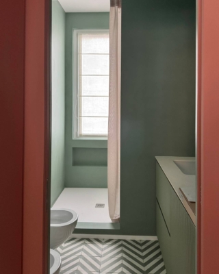 In questo bagno caratterizzato dall’uso del colore verde la doccia, con il piatto tagliato a misura realizzato in una miscela di quarzi, rimane posizionata sotto la finestra e separata dal resto del bagno grazie a un muretto laterale. Sotto la finestra è stata creata una nicchia utile per riporre shampoo e prodotti. Prima del muro della doccia c’è il lavabo a incasso con armadietto che contiene anche la lavatrice, nascondendola completamente.