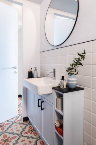 Un lavandino semincasso di misura contenuta, ma di forma rettangolare, è la soluzione scelta per questo bagno molto stretto: il mobile lavabo laccato in colore azzurro ghiaccio misura solo 30 centimetri di profondità. I dettagli neri, come le maniglie e la cornice dello specchio, lo arricchiscono con un contrasto raffinato.