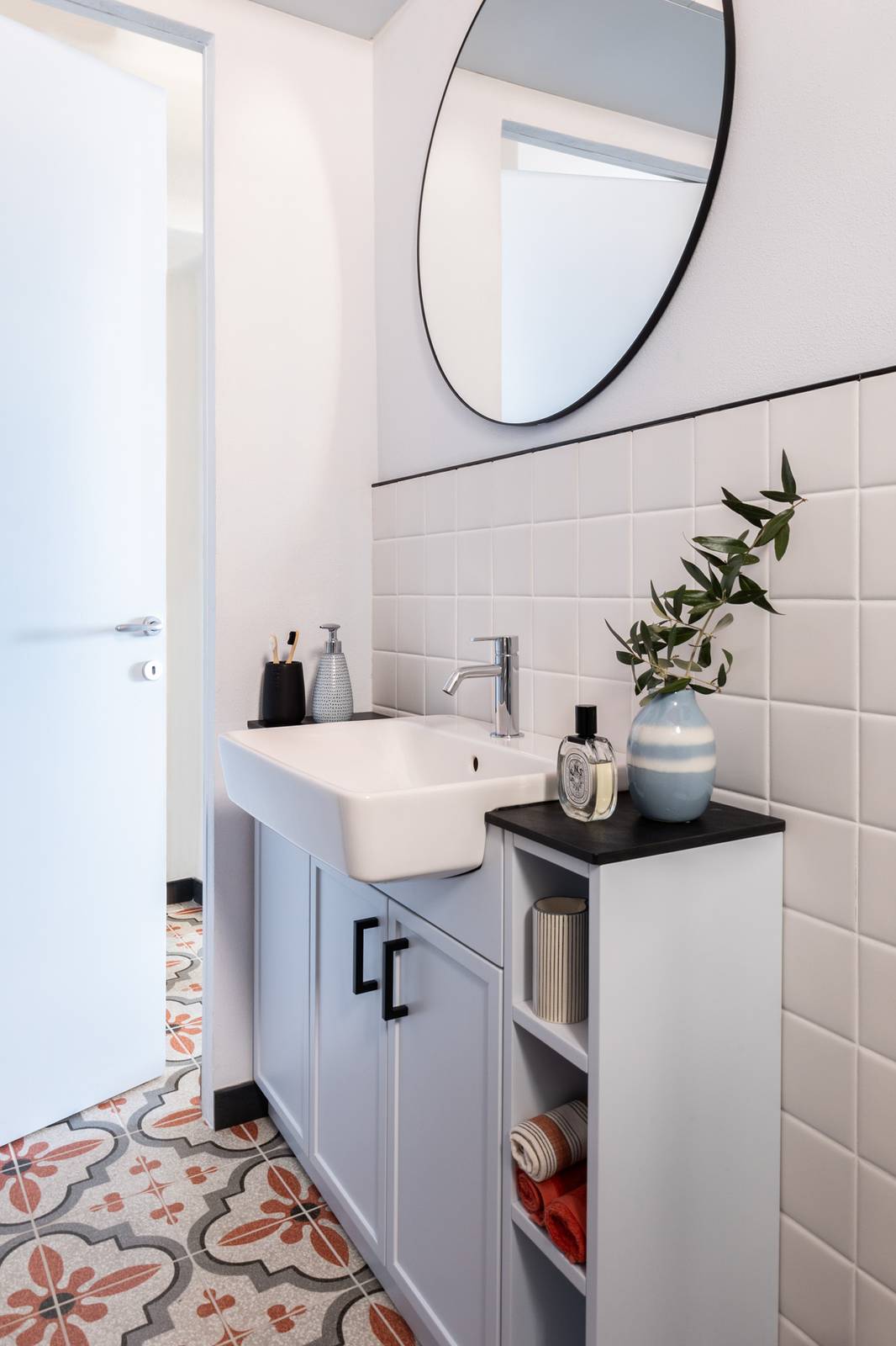 Un lavandino semincasso di misura contenuta, ma di forma rettangolare, è la soluzione scelta per questo bagno molto stretto: il mobile lavabo laccato in colore azzurro ghiaccio misura solo 30 centimetri di profondità. I dettagli neri, come le maniglie e la cornice dello specchio, lo arricchiscono con un contrasto raffinato.