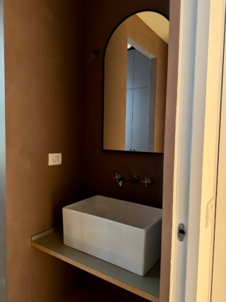 In questo bagno il lavatoio geometrico e capiente aggiunge  una nota grintosa e: è abbinato a un bello specchio dalla forma curvilinea con  una luce di design anni ’50. Anche il colore caldo e materico delle pareti contribuisce a creare un effetto finale che non assomiglia a una lavanderia.