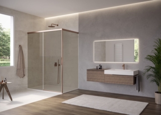 Ha telaio parziale la cabina doccia natura 4000 di Duka con porta scorrevole combinata a un elemento laterale e profili con finitura copper pearl. Senza il profilo verticale si alleggerisce l’impatto visivo. Il vetro, nella foto in finitura bronze, è fissato alla parete tramite elementi di supporto discreti. Misura L 130 x H 200 cm, l’elemento laterale è largo 60 cm. www.duka.it – Cersaie 2026, Pad. 21, Stand A69/B68