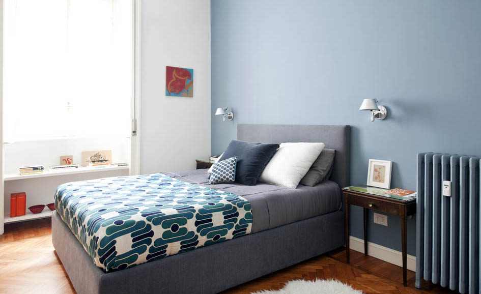 Un vecchio tavolino diventa comodino accanto aun moderno letto tessile.