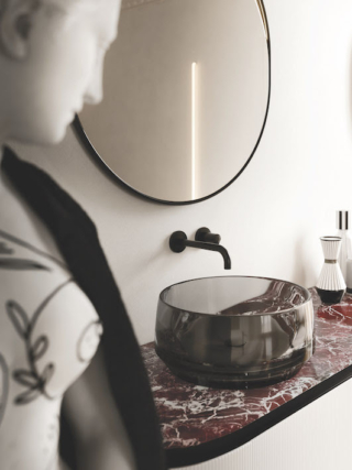 Brandy è un lavabo da appoggio compatto, che prende il nome e le proporzioni dal bicchiere da degustazione: una base spessa e solida, pareti che salgono morbide e un bordo netto ne definiscono la silhouette essenziale e riconoscibile. Nella versione trasparente fumé, il fondo pieno conferisce consistenza, richiamando la solidità di un bicchiere di cristallo, mentre le pareti lasciano filtrare la luce e creano un dialogo con la superficie sottostante. Il materiale e il colore del top rimangono infatti visibili attraverso il lavabo, diventando parte della sua stessa espressività, mentre la trasparenza permette di vedere l’acqua anche dall’esterno. Appoggiato sul piano, accanto a vasi e flaconi di uso quotidiano, Brandy assume così il carattere di un oggetto tra gli oggetti, fino a diventare un vero e proprio complemento d'arredo. Alla leggerezza visiva della versione trasparente si affianca la variante piena e opaca in Ocritech, pensata per chi ricerca una presenza più materica. Brandy è un lavabo da appoggio compatto, che prende il nome e le proporzioni dal bicchiere da degustazione: una base spessa e solida, pareti che salgono morbide e un bordo netto ne definiscono la silhouette essenziale e riconoscibile. Nella versione trasparente fumé, il fondo pieno conferisce consistenza, richiamando la solidità di un bicchiere di cristallo, mentre le pareti lasciano filtrare la luce e creano un dialogo con la superficie sottostante. Il materiale e il colore del top rimangono infatti visibili attraverso il lavabo, diventando parte della sua stessa espressività, mentre la trasparenza permette di vedere l’acqua anche dall’esterno. Appoggiato sul piano, accanto a vasi e flaconi di uso quotidiano, Brandy assume così il carattere di un oggetto tra gli oggetti, fino a diventare un vero e proprio complemento d'arredo. Alla leggerezza visiva della versione trasparente si affianca la variante piena e opaca in Ocritech, pensata per chi ricerca una presenza più materica.