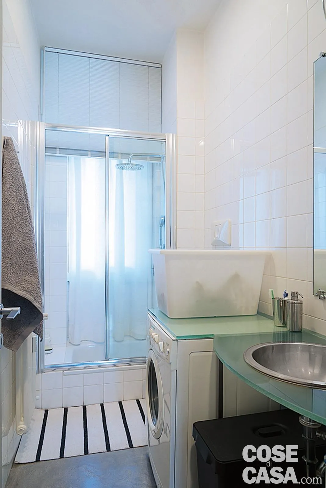 Bagno con specchio con struttura in metallo grigio lavabo in vetro su  supporti cromati cabina doccia con divisorio in vetro pavimento  piastrellato e finestra in alluminio bianco