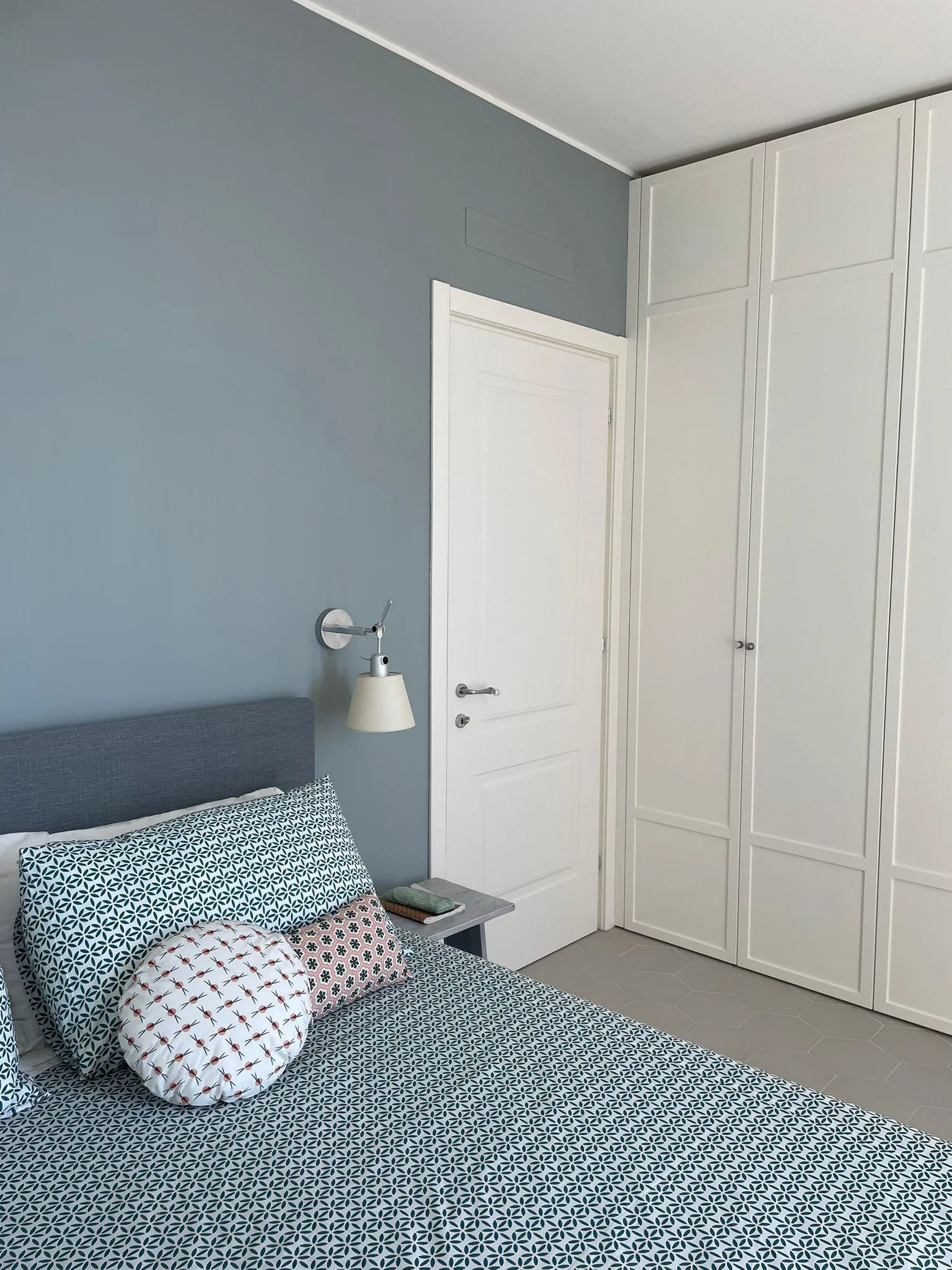 Una camera da letto con un letto e uno sgabello davanti a una parete con  sopra un lampadario.